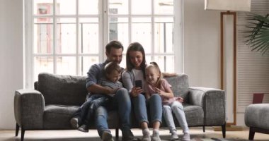 Dört kişilik mutlu bir aile akıllı telefon kullanıyor. Kanepede rahatlayın.