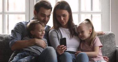 Neşeli ebeveynler ve çocuklar cep telefonunda komik bir uygulama kullanarak gülüyorlar.