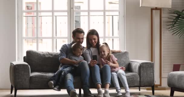 Ευτυχισμένη οικογένεια των τεσσάρων χρησιμοποιώντας smartphone χαλαρώστε στον καναπέ — Αρχείο Βίντεο