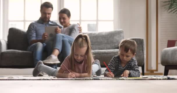 Enfants dessinant sur le sol parents relaxant sur canapé à la maison — Video