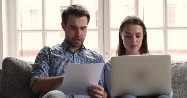 Серйозний молодий чоловік і дружина використовують платіжні рахунки ноутбуків онлайн — стокове відео