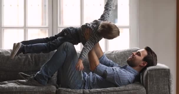 Divertido niño hijo volando en papás manos jugando en casa — Vídeo de stock