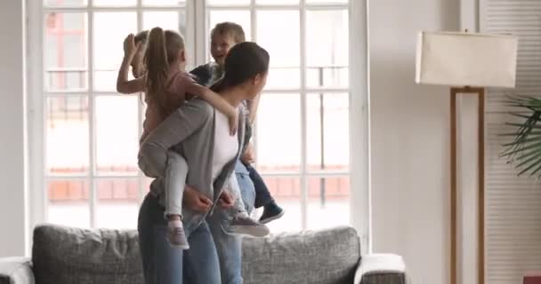 Mutlu ebeveynler oturma odasında oynayan küçük çocukları sırtında taşıyor. — Stok video