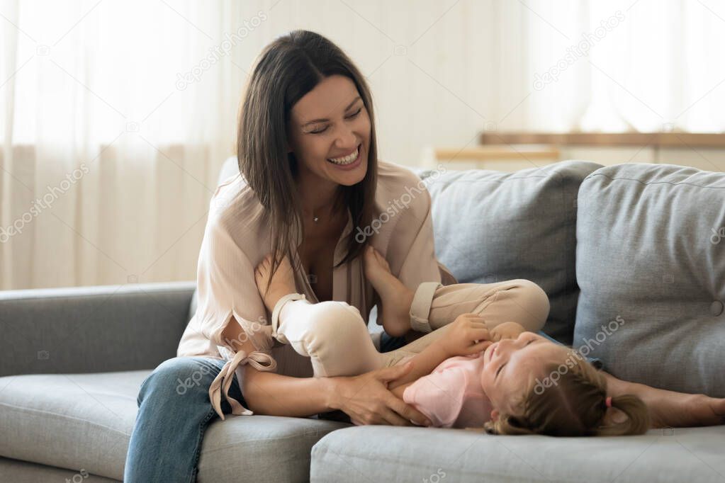 Girl lying on back while happy mother tickling her.