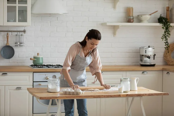 Mujer de 30 años inclinada sobre la mesa, extendiendo la masa . —  Fotos de Stock