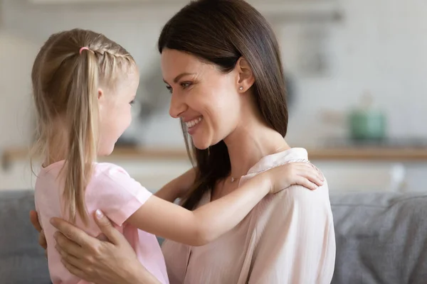 Lilla söta flicka som lägger händerna på leende mammor axlar. — Stockfoto