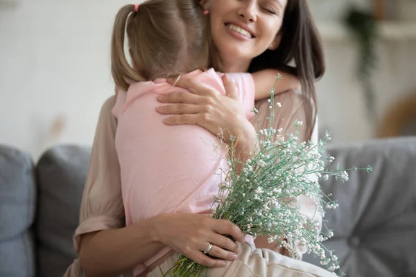 Cropped image focus on flowers, excited young mother cuddling daughter.
