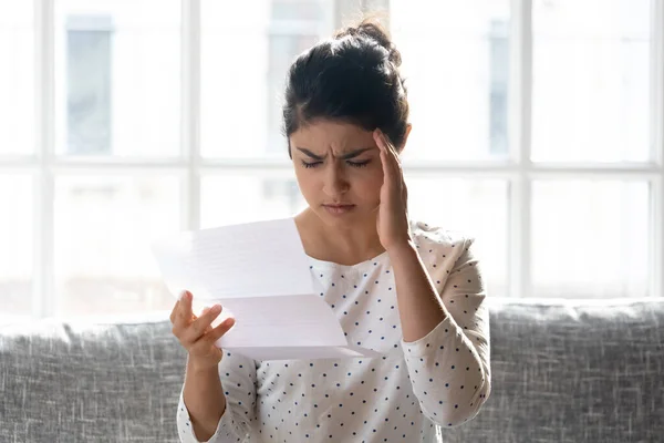 Stressed millennial indian woman reading paper letter with bad news.
