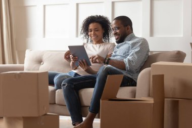 African couple sit on couch near boxes using tablet computer clipart