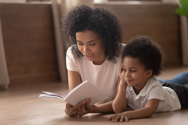 Afrikaanse moeder voorlezen sprookje naar zoon liggend op de vloer — Stockfoto