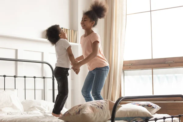 Брат и сестра смешанной расы держатся за руки, прыгая на кровати — стоковое фото