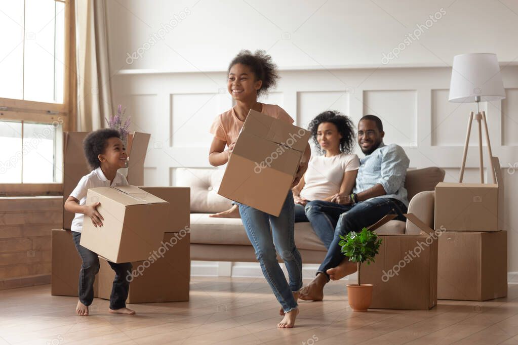 Active african kids running with carton boxes in living room