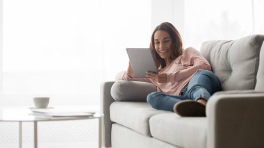 Gülümseyen kız kanepede oturup tablette video izliyor.