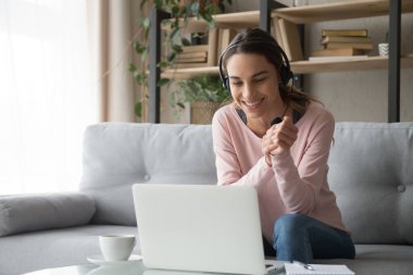Gülümseyen kadın evdeki koltukta oturmuş Webinar 'ı seyrediyor.
