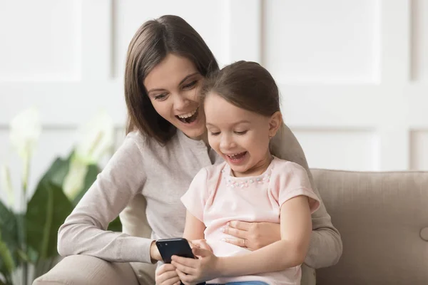 Emocionado jovem mãe e pequena filha jogar smartphone juntos — Fotografia de Stock