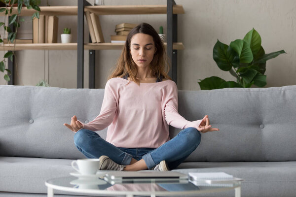 Calm woman relax on couch meditating practicing yoga