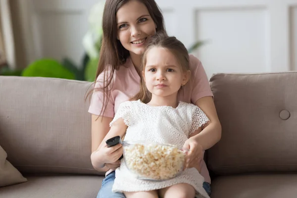 Little girl watch TV with young mom eating popcorn