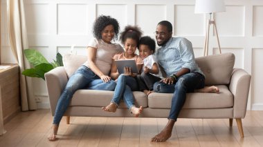Afrikalı bir aile kanepede dinlenirken tablet bilgisayar kullanıyor.
