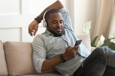 Gülümseyen melez adam evde kulaklıkla müzik dinliyor.