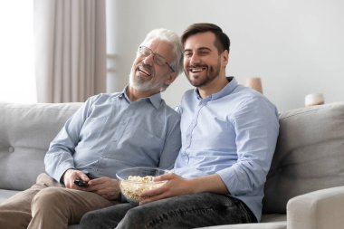 Mutlu yetişkin baba ve oğul televizyon programı izliyorlar.