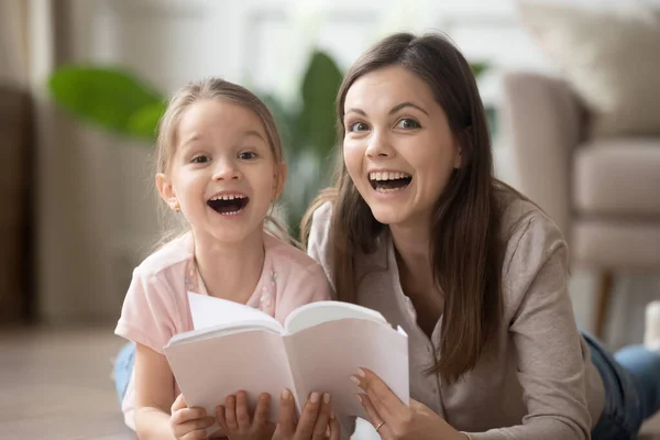 Sonriente mamá y su hija tumbados en el piso de lectura libro juntos —  Fotos de Stock