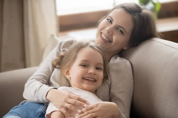 Porträtt av leende mamma och liten dotter avkopplande på soffan — Stockfoto