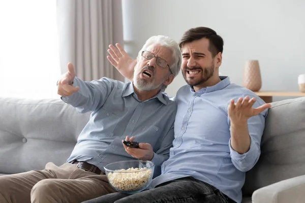 Unhappy old father and son watching tv, bad football match