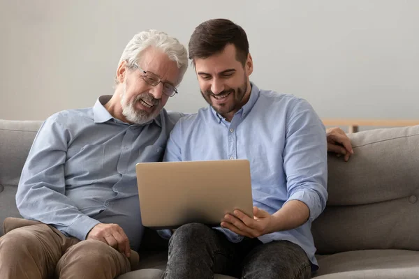 Usmívající se starý otec a dospělý syn při pohledu na obrazovce notebooku — Stock fotografie