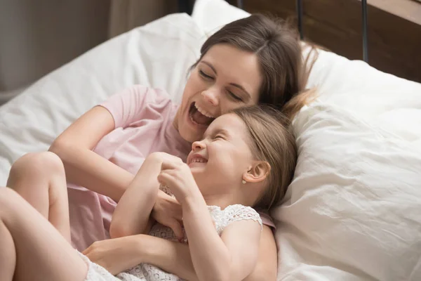 Sonriente mamá tener divertido jugando con poco hija en dormitorio —  Fotos de Stock