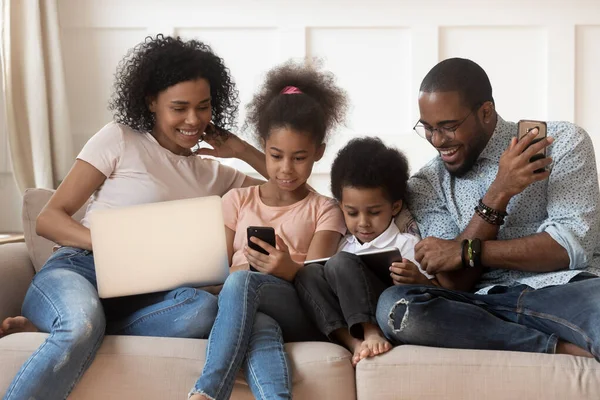 Famiglia africana e bambini utilizzando diversi gadget seduti sul divano — Foto Stock