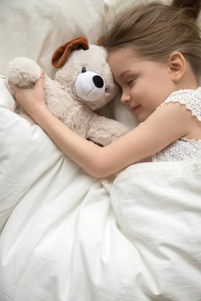 Niña durmiendo abrazando osito de peluche en dormitorio blanco — Foto de Stock