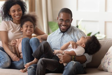 Küçük çocuklu Afrikalı bir aile kanepede oturup eğleniyor.