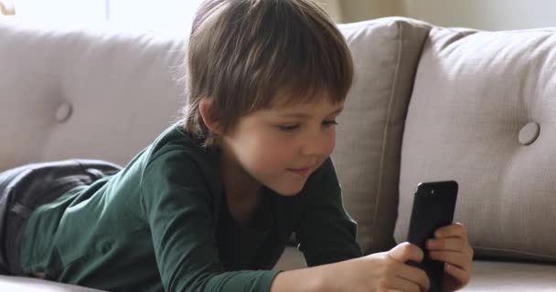 Nieuwsgierige schattige schooljongen houden smartphone kijken video 's alleen thuis — Stockvideo
