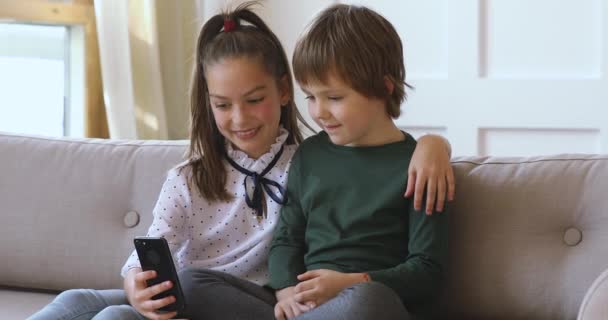 Duas crianças menino menina aprendendo usando smartphone juntos no sofá — Vídeo de Stock