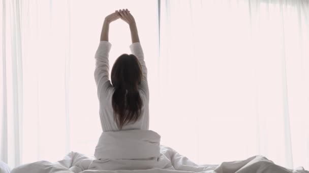 Glad ung dam stretching vakna sitter i mysig säng — Stockvideo