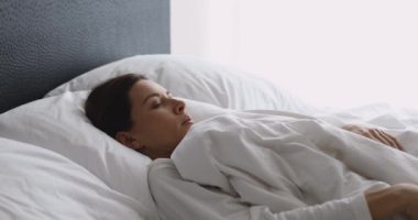 Hasta genç kadın uyanıyor. Yatağa otur ve sırt ağrısı hisset.