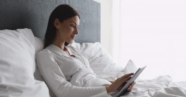 Joven sonriente hermosa mujer usando tableta digital relajarse en la cama — Vídeos de Stock