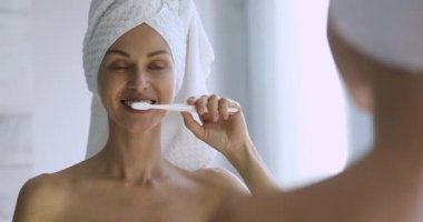 Sağlıklı dişlerini fırçalayan mutlu genç bayan aynaya bakıyor.