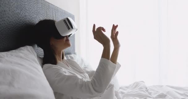 Woman wearing vr glasses using virtual reality interface in bed — Stock Video