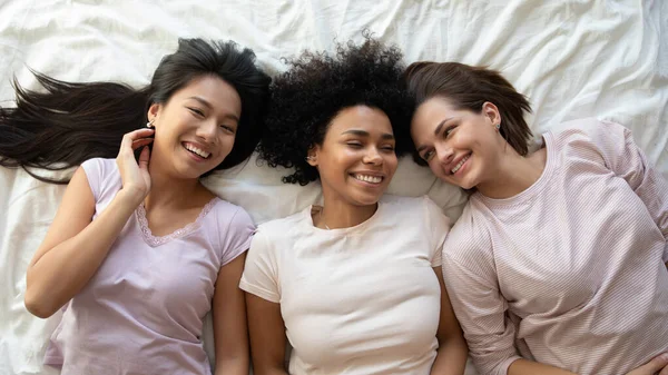 Três felizes engraçado multiétnico senhoras amigos rindo deitado na cama — Fotografia de Stock