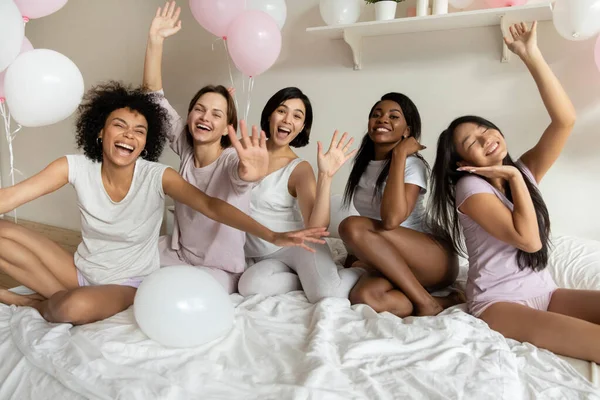 Heyecanlı kızlar balonlarla yatakta kameraya bakıyorlar. — Stok fotoğraf