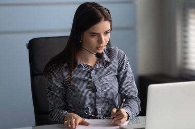 Kulaklıklı kadın çalışan Webinar 'ı izlerken not alıyor