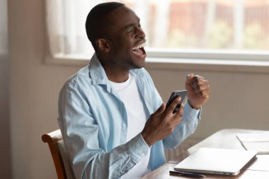 Coşkulu Afrikalı Amerikalı adam cep telefonuyla heyecanlanıyor.