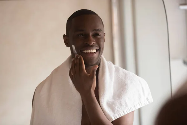 African American man apply facial cream looking in mirror — Stock Photo, Image