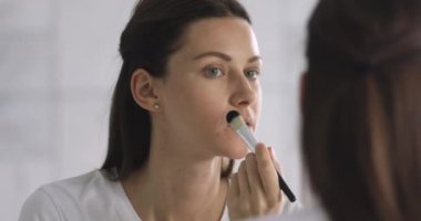 Elinde fırça tutan çekici genç bir kadın yüzüne temeli vurur.