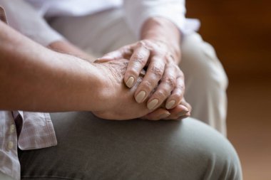 Doktor, yaşlı erkek hastanın kırışık ellerini tutuyor..