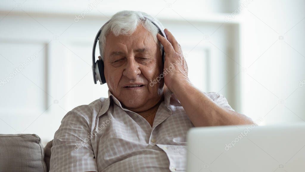 Older happy man wearing wireless headphones, enjoying favorite music.