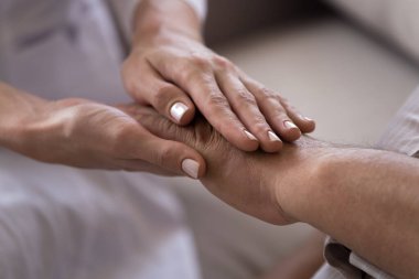 Genç bayan doktor, yaşlı erkek hastanın elini tutuyor..