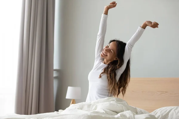 Wanita yang duduk di tempat tidur meregangkan otot lengannya setelah tidur — Stok Foto