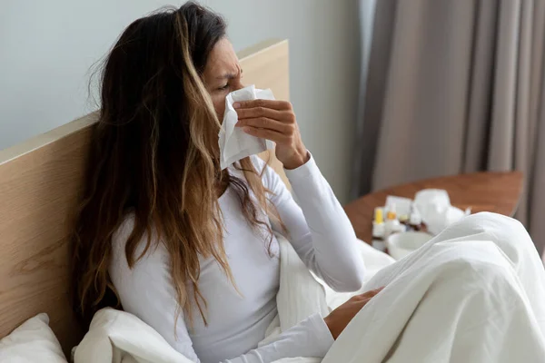 Sick woman holding paper handkerchief wiping blowing runny nose